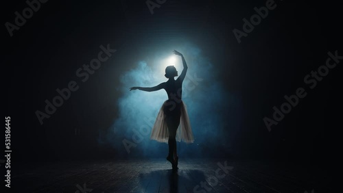Silhouette of ballerina in backlight of spotlights. Graceful ballet dancer spins on toes in pointe shoes