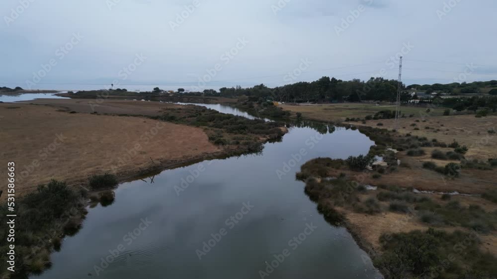 medium altitude drone on a cloudy day slowly rotating over reflective still body of water with birds passing by. medium altitude drone on a cloudy day slowly rotating over reflective still body of water with birds passing by.