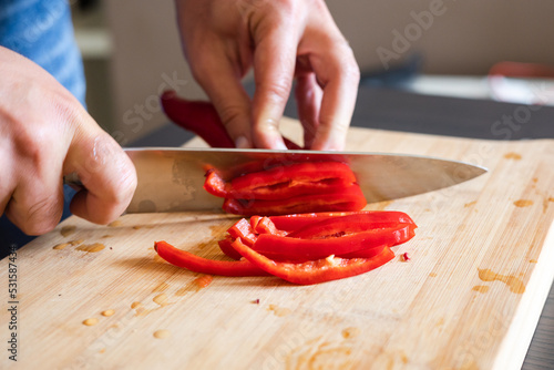 man hands cutting red pepper close up on wooden board