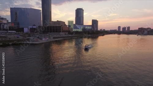 Aerial shot of river in city against sky during sunset, A boat with a guy and a girl floats on the river, People are walking on the embankment, boats are floating on the river. Dusk wonderful colors o