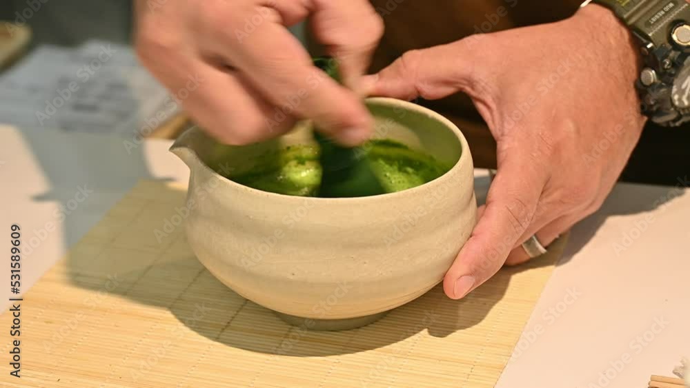 Close up of barista using a bamboo whisk for stirring and mixing Matcha tea powder with water and milk in Japanese bowl. Close up of barista using a bamboo whisk for stirring and mixing Matcha tea powder with water and milk in Japanese bowl.