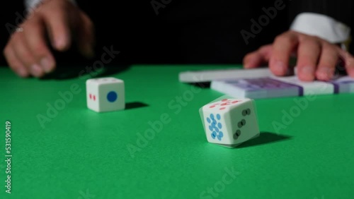 The hand rolls the dice and puts a wad of money on the green gaming table. The effect of bifurcation. White Dice Transition, devil's bones, Transition, Casino dice, Falling Dice