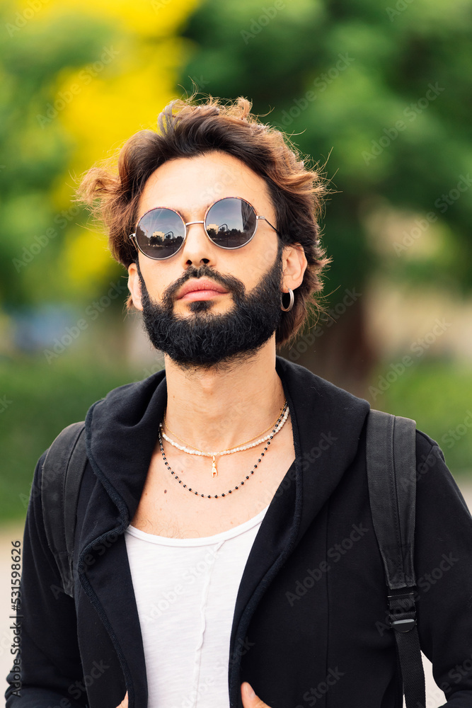 vertical portrait of a stylish young man with beard and sunglasses looking at camera, concept of youth and urban life style vertical portrait of a stylish young man with beard and sunglasses looking at camera, concept of youth and urban life style