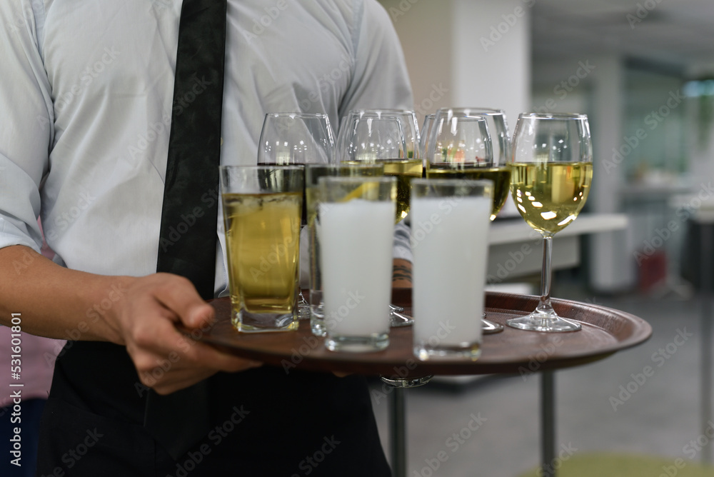 The waiter serves drinks at the party, there is wine and other alcoholic beverages on the tray