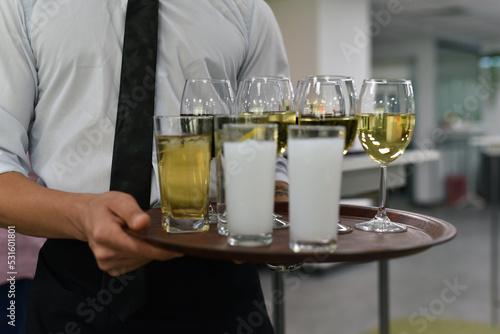 The waiter serves drinks at the party, there is wine and other alcoholic beverages on the tray