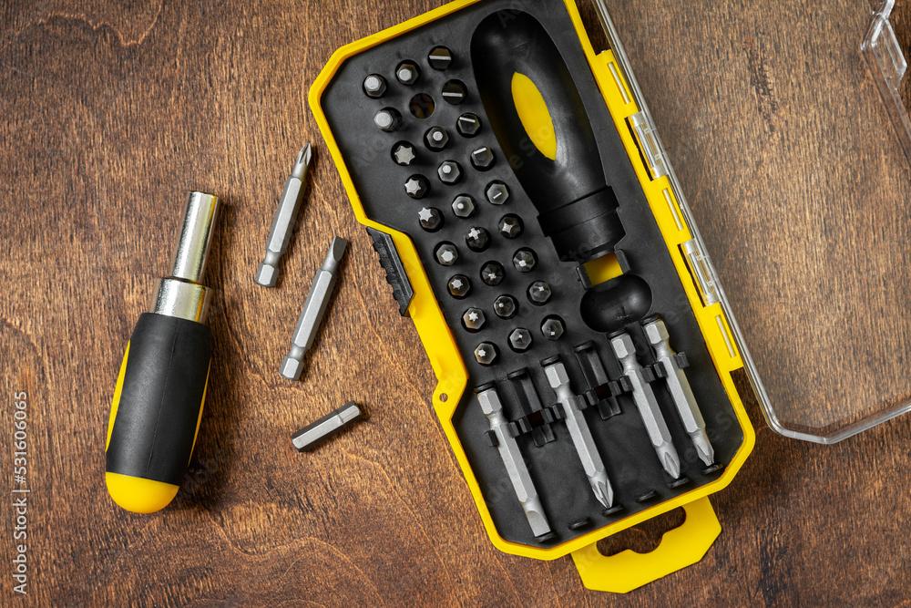 A set of small screwdrivers on a brown wooden table. Bits of different sizes in an open case. Top view