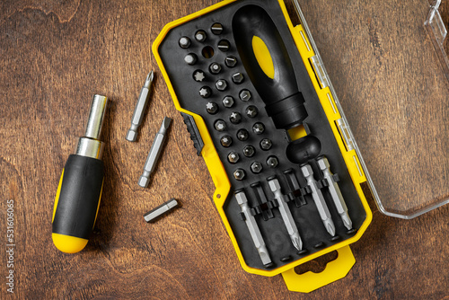 Obraz na płótnie A set of small screwdrivers on a brown wooden table. Bits of different sizes in an open case. Top view w salonie
