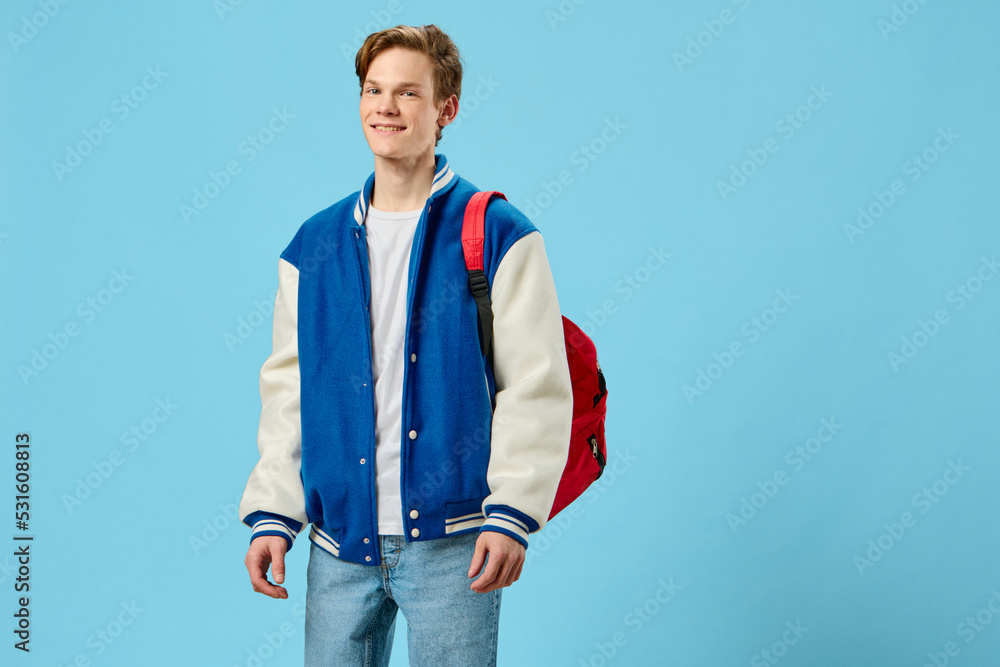 Fototapeta premium horizontal portrait of a handsome, joyful student guy with a red backpack on his shoulder, looking at the camera
