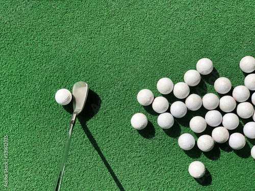 Group of partial appear golf balls on practice artificial grass mat with an iron address at one ball under morning sunlight.