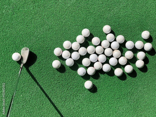 Group of practice golf balls on practice artificial grass mat with one club iron address at one ball under morning sunlight.