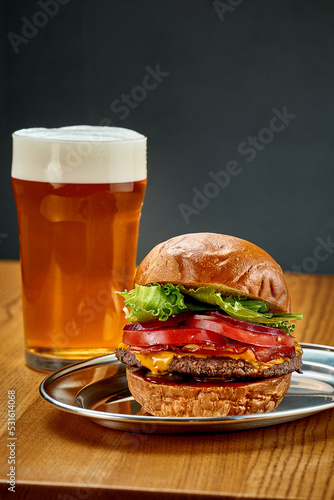 A big juicy burger with vegetables and a glass of beer. Close-up, selective focus
