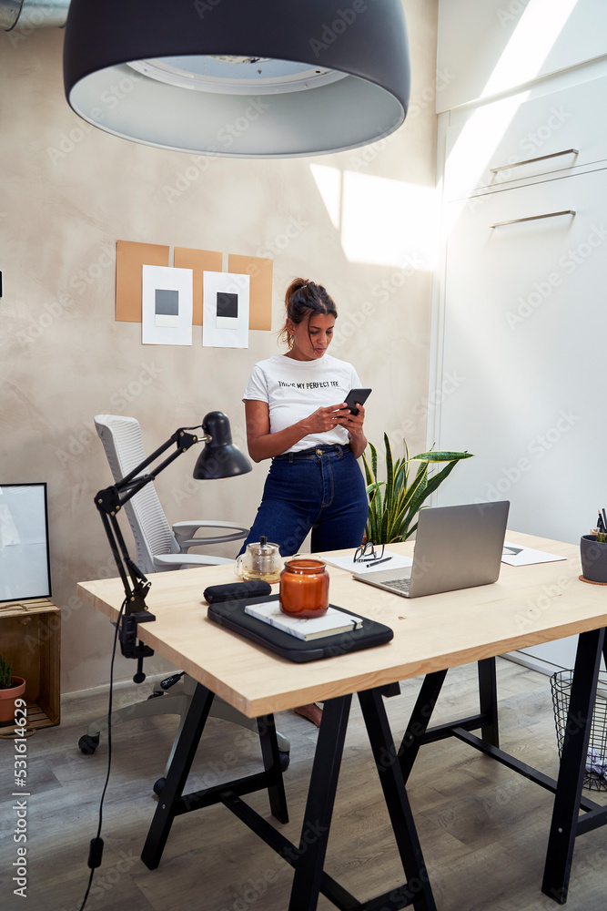 Freelancer text messaging through mobile phone standing at home office Freelancer text messaging through mobile phone standing at home office