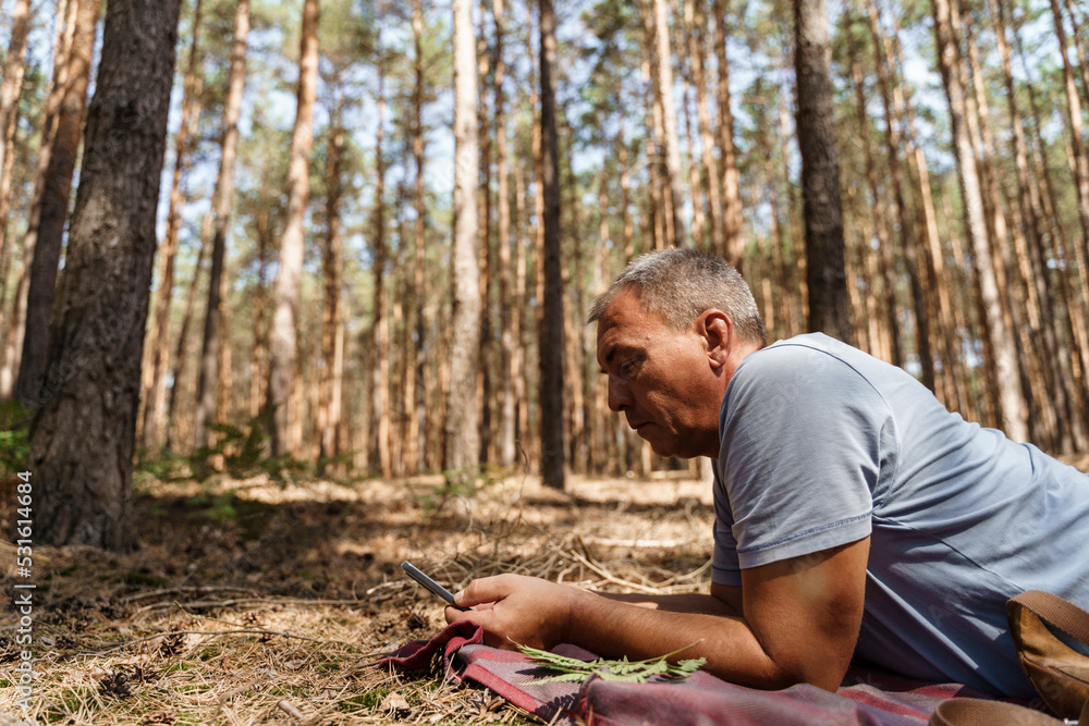 Mature man using smart phone lying in forest Mature man using smart phone lying in forest