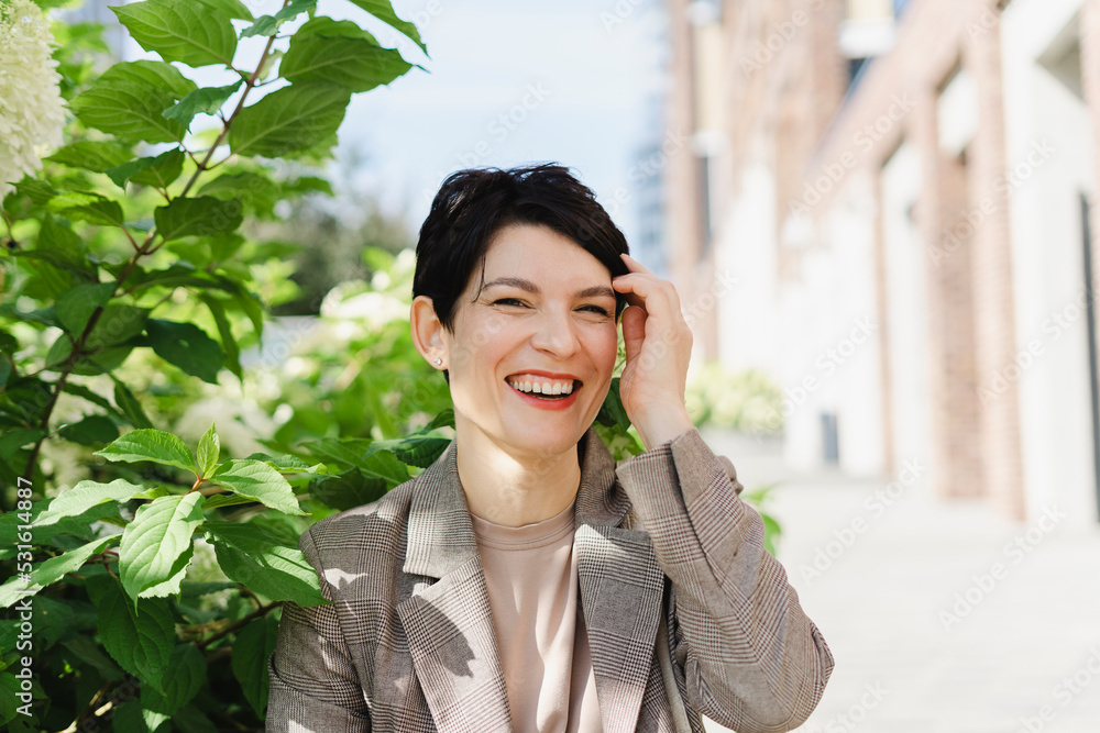 Cheerful businesswoman touching hair by plant on sunny day Cheerful businesswoman touching hair by plant on sunny day