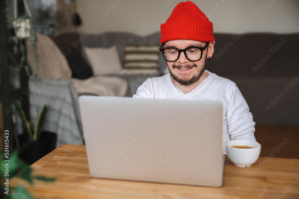 Smiling man wearing knit hat using laptop at home Smiling man wearing knit hat using laptop at home