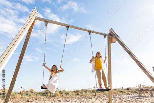 Cheerful girl with brother playing on swing at beach photo