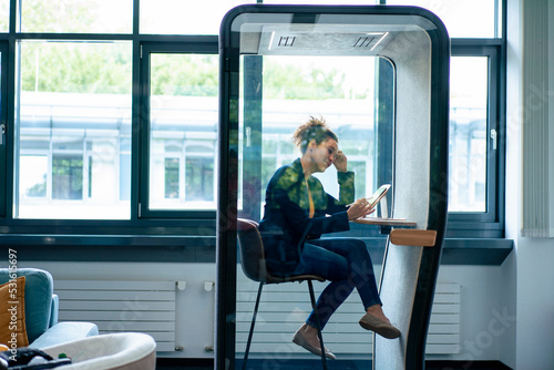 Businesswoman working on tablet computer sitting in soundproof cabin