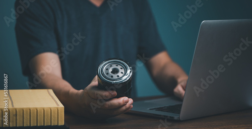 Businessman holding automotive oil filter in hand and buying on online marketing website and social media store form laptop computer.