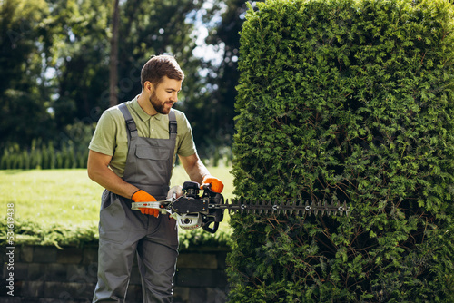 Foto Man worker cutting bushes with an electric saw in the yard