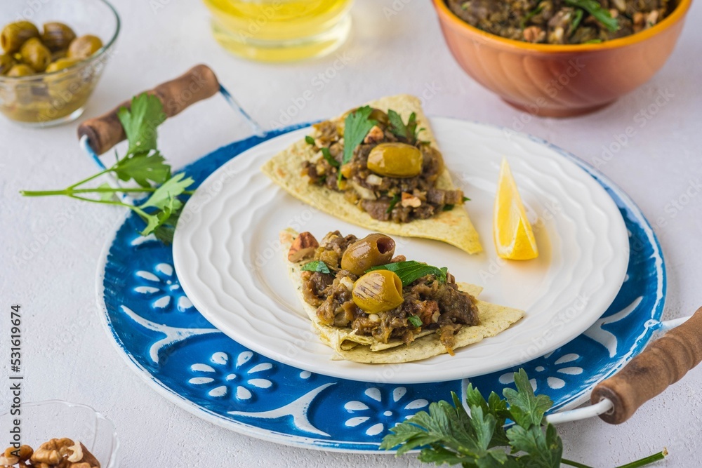 An appetizer, a salad of baked eggplant, onions, herbs and spices on tortillas on a white plate on a light concrete background. Recipes for eggplant. An appetizer, a salad of baked eggplant, onions, herbs and spices on tortillas on a white plate on a light concrete background. Recipes for eggplant.