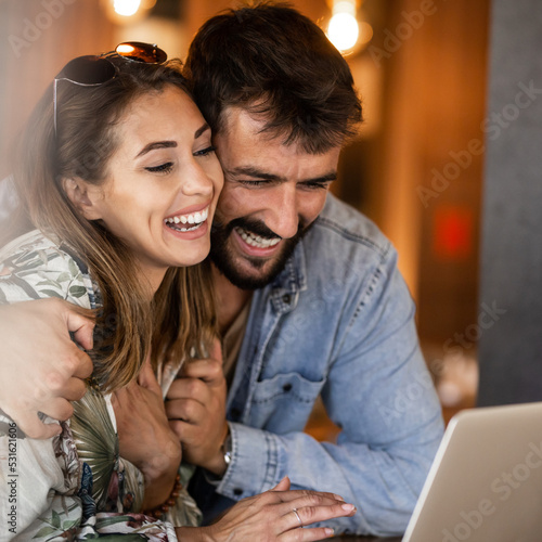 Happy couple using laptop at cafe enjoying time together Smiling looking at each other 