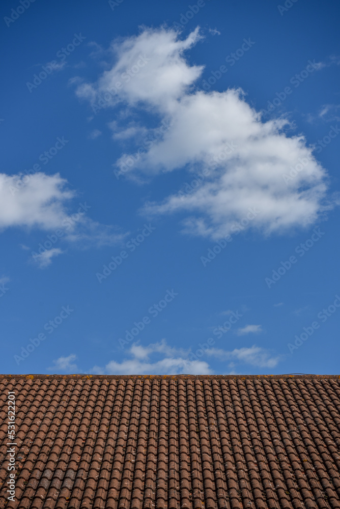 Naklejka premium Abstract image of a brick tiled roof top contrasting with a bright blue sky with white clouds.