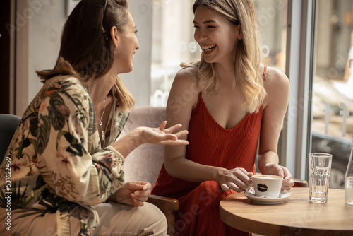 Stylish young women having friendly meeting with cups of coffee while sitting at table and chatting