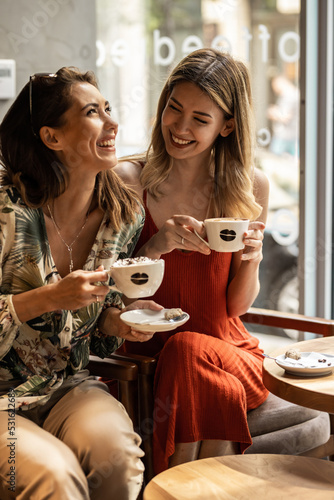Beautiful happy women talking and laughing while drinking coffee together in coffee shop.