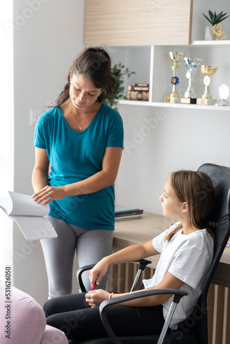 Pregnant mother and daughter sitting in the room and talking, mother revising daughters homework