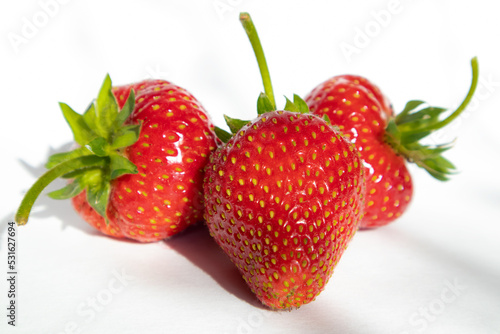 Three strawberries on a white background in sunlight. Isolate.