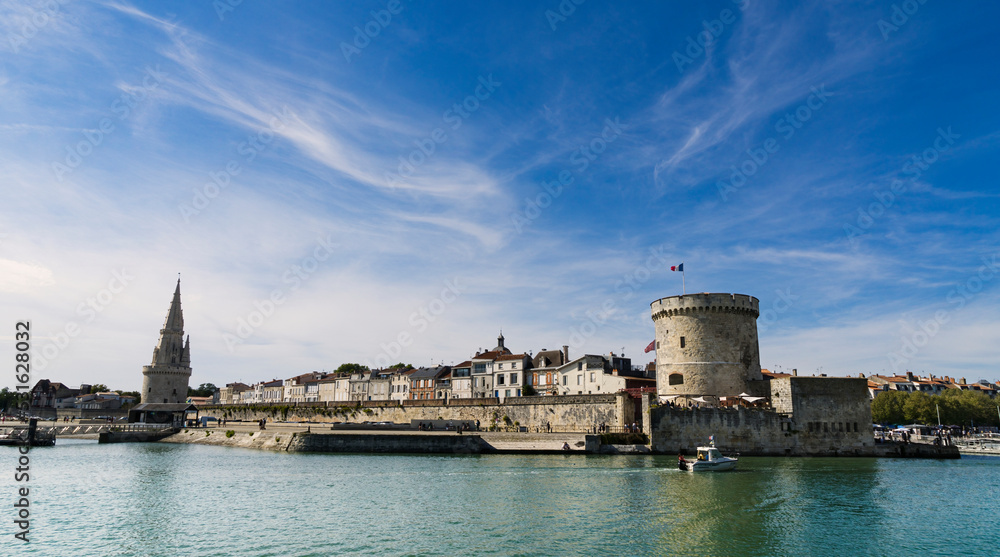 View of the entrance to the old port of the French city of La Rochelle with the medieval tower and blue sky with light clouds.