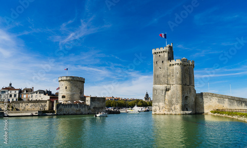 View of the entrance to the old port of the French city of La Rochelle with the two medieval towers and blue sky with light clouds.