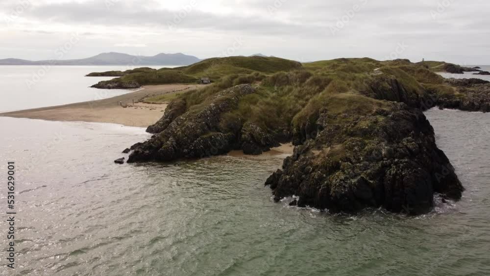 Aerial low orbit view Ynys Llanddwyn island Anglesey coastal walking trail with Snowdonia mountains across the Irish sea Aerial low orbit view Ynys Llanddwyn island Anglesey coastal walking trail with Snowdonia mountains across the Irish sea