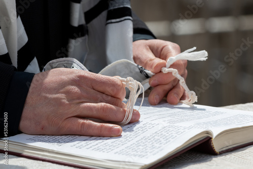 Closeup of a Jewish man praying while holding the strings or tzitzit on his tallit in his hand and reciting the shema yisrael. photo