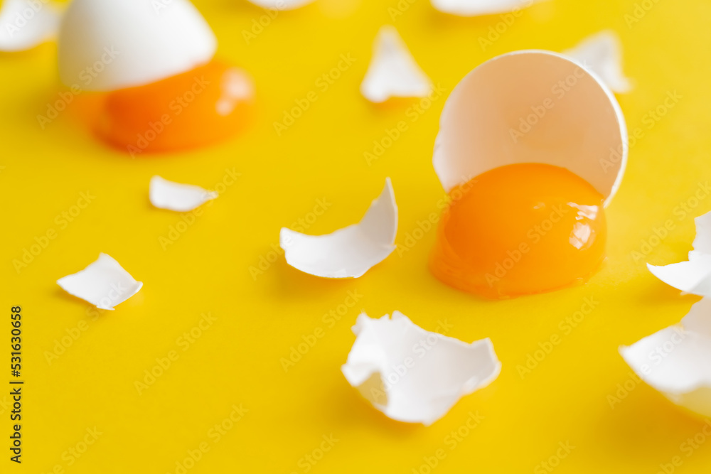 Close up view of fresh yolk and cracked egg shells on yellow surface. Close up view of fresh yolk and cracked egg shells on yellow surface.