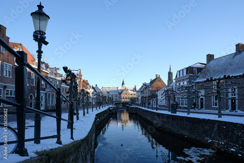 Blue hour winter scene with snow and ice in the canal in old city center of Amersfoort, Netherlands. Overlooking the streets Grote Spui and Kleine Spui with museum Flehite in the background