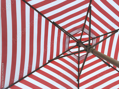 abstract under to top partial view of a big size wood structure with red and white stripe in hexagon fabric shield outdoor umbrella