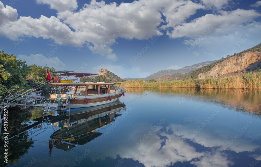 The rock-cut temple tombs of the ancient city of Kaunos in Dalyan, Muğla, Turkey. Beautiful view of Dalyan river with reed beds, excursion boats and carved tombs in the background.