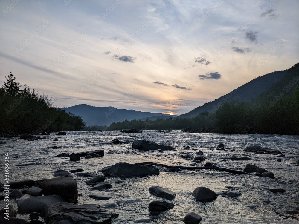Beautiful cloudy sky at sunset over the river. The high bank of the river is overgrown with grass. Beautiful cloudy sky at sunset over the river. The high bank of the river is overgrown with grass.
