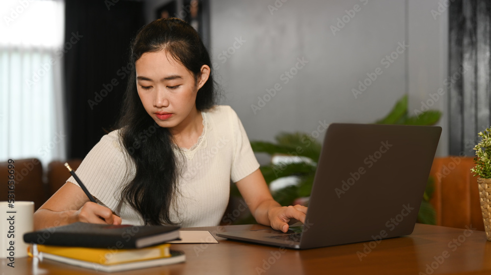 Young asian lady study online on laptop and writing important information on notebook. Education, e-learning, distance training Young asian lady study online on laptop and writing important information on notebook. Education, e-learning, distance training