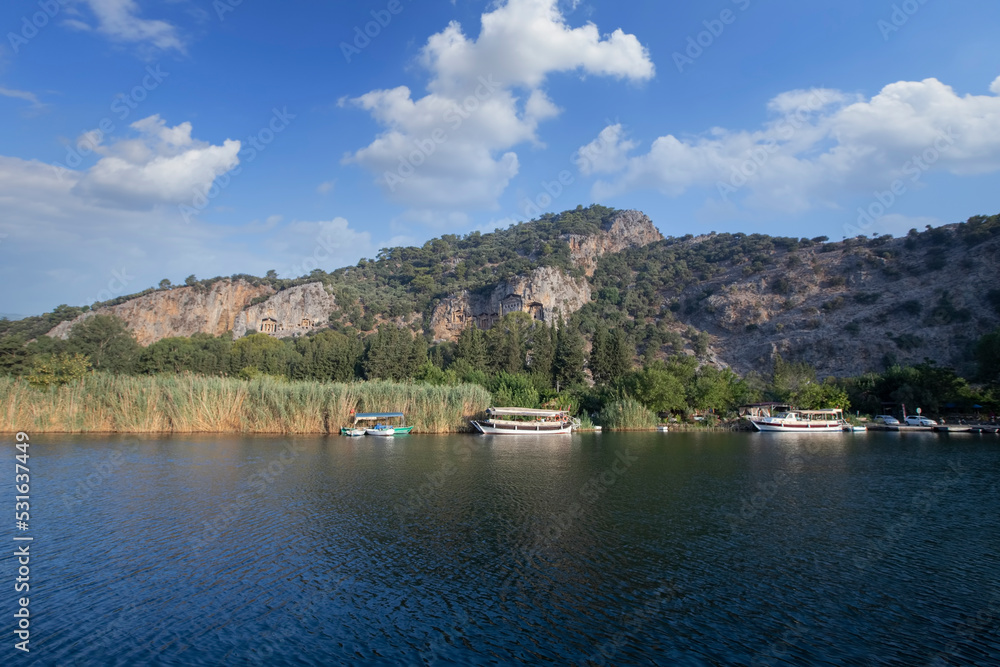 The rock-cut temple tombs of the ancient city of Kaunos in Dalyan, Muğla, Turkey. Beautiful view of Dalyan river with reed beds, excursion boats and carved tombs in the background.