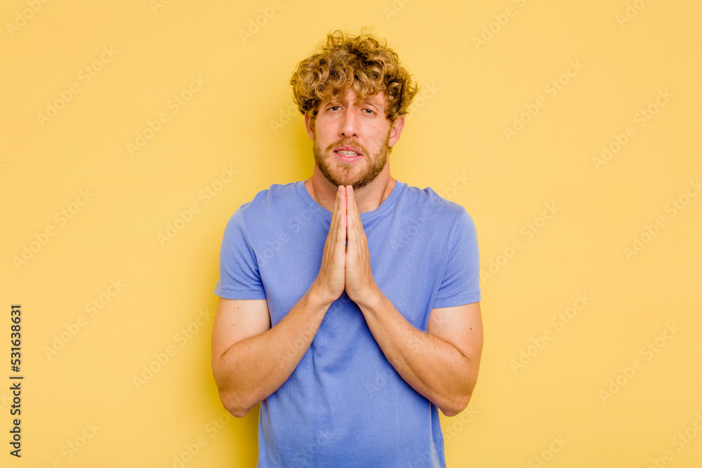 Young caucasian man isolated on yellow background holding hands in pray near mouth, feels confident. Young caucasian man isolated on yellow background holding hands in pray near mouth, feels confident.