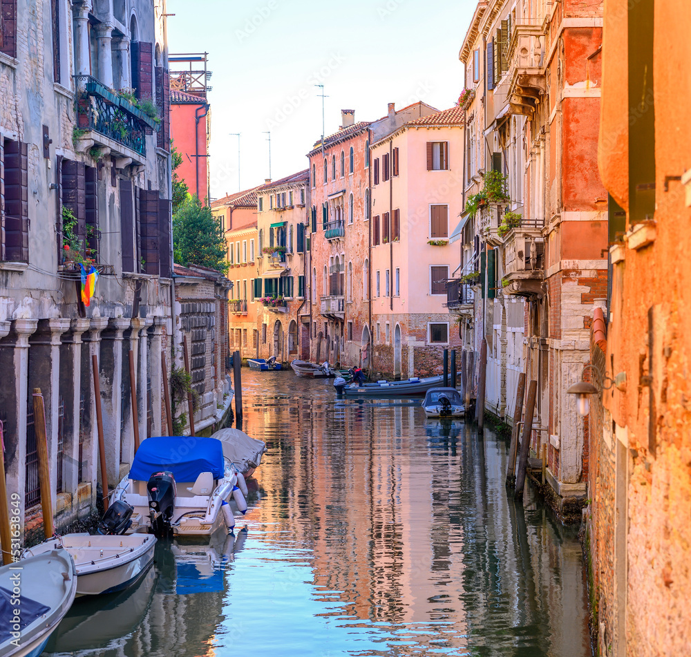 View on the narrow cozy streets of the canals with parked boats in Venice, Italy. Architecture and landmark of Venice.