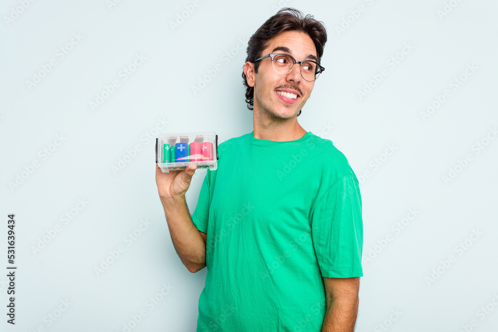 Young hispanic man holding battery box isolated on white background looks aside smiling, cheerful and pleasant. Young hispanic man holding battery box isolated on white background looks aside smiling, cheerful and pleasant.