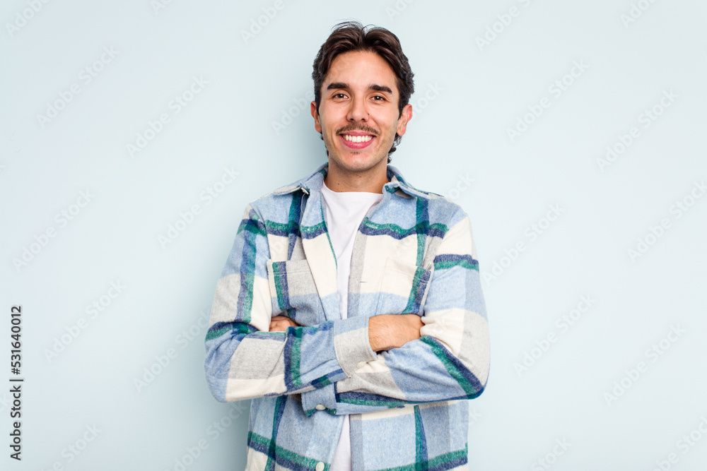 Young hispanic man isolated on blue background who feels confident, crossing arms with determination. Young hispanic man isolated on blue background who feels confident, crossing arms with determination.