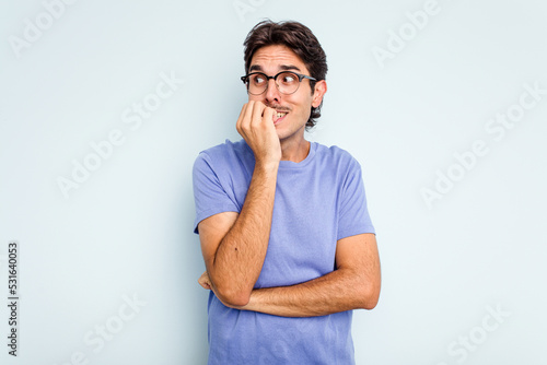 Young hispanic man isolated on blue background biting fingernails, nervous and very anxious.