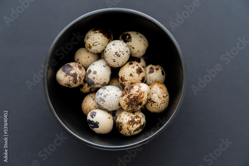 Top view of fresh quail eggs in bowl on black background.