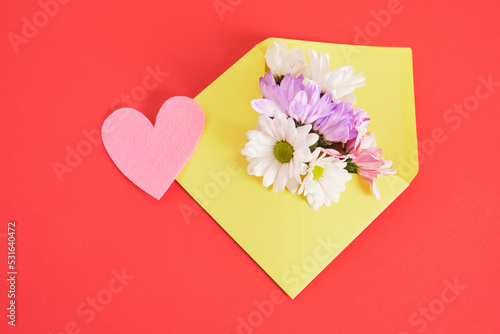 flower, mock up yellow envelope and pink felt heart on red background