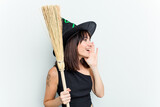 Young caucasian woman dressed as a witch holding a broom isolated on blue background shouting and holding palm near opened mouth.