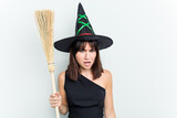 Young caucasian woman dressed as a witch holding a broom isolated on blue background screaming very angry and aggressive.